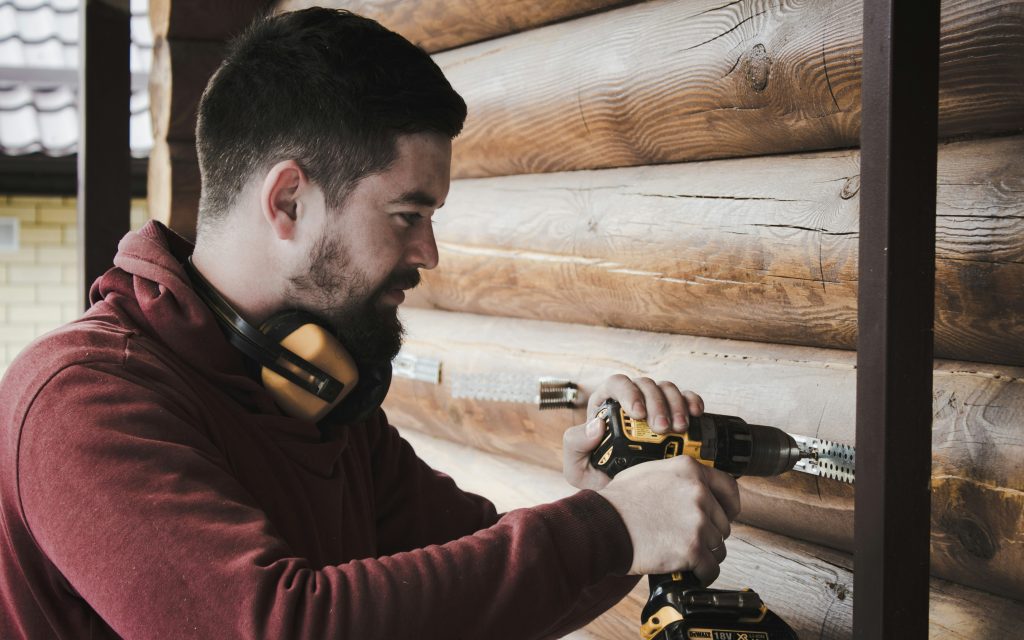 Construction worker using a power drill on a wooden log house
